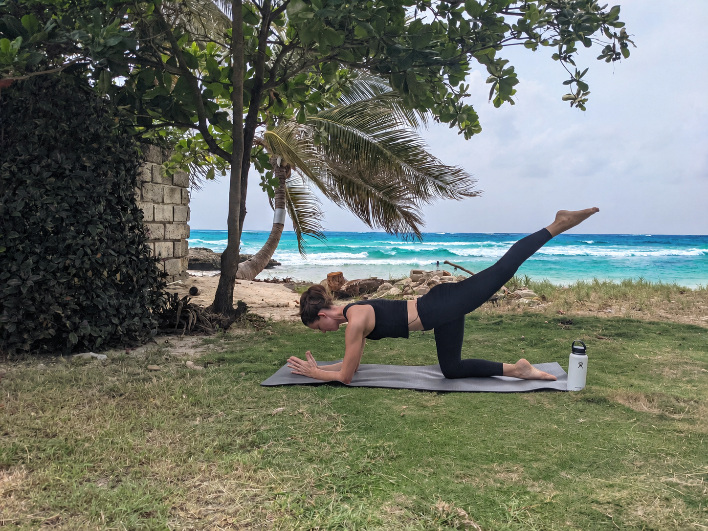 Joanie demonstrating a Pilates strength exercise outdoors beside the sea.
